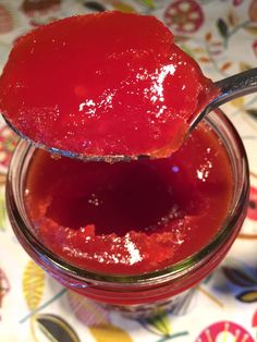 a spoon full of jelly sitting on top of a glass jar filled with red liquid