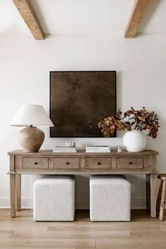 a wooden table topped with two white vases next to a painting on the wall