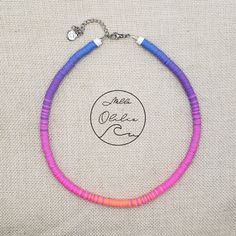 a pink and blue beaded necklace is displayed on a piece of fabric with a silver clasp