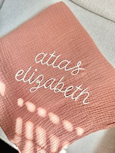 a pink blanket with the words atlas elizabeth written in white on it, sitting on a couch