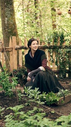 a woman is sitting on a bench in the woods with trees and plants around her