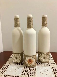 three white bottles sitting on top of a table next to each other with flowers in them