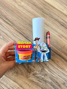 a hand is holding a toy story book with crayons and pencils next to it