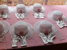 many hats and gloves sit on a pink table cloth with white lace around the edges