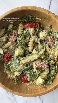 a pasta salad with spinach and tomatoes in a wooden bowl on a marble table