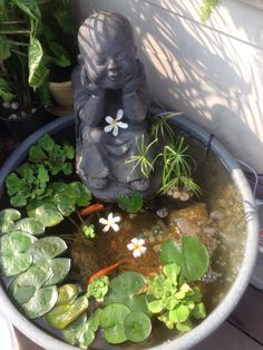 a small buddha statue sitting on top of a planter filled with water and plants