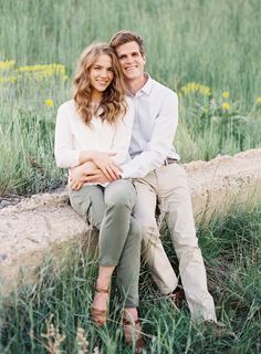 a man and woman sitting next to each other on a rock in a field with tall grass