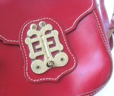 "Red leather bag with Asian flair. Bag is made of red Gahna Cowhide and has a large brass Asian-style medallion on the flap. There is a long adjustable shoulder strap which can be doubled up to carry as a handbag. At full length it is long enough to wear as a cross body bag. Thick leather is on the stiff side. I believe this to be from the 1960s but could be older based on some of the other clothing items that I found at this rad estate sale. Measures approximately 9\" x 9\" x 2.5\". The top sti Elegant Red Shoulder Bag With Brass Hardware, Red Shoulder Bag With Brass Hardware For Everyday Use, Elegant Red Bag With Brass Hardware, Red Leather Satchel With Metal Hardware, Red Travel Bag With Brass Hardware, Red Shoulder Bag With Metal Hardware For Travel, Vintage Red Handmade Satchel, Vintage Handmade Red Satchel, Red Leather Shoulder Bag With Metal Hardware