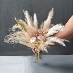 a person holding a bouquet with feathers and flowers in their hand, on a table