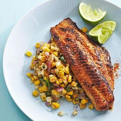 a white plate topped with fish and corn next to lime wedges on a blue table