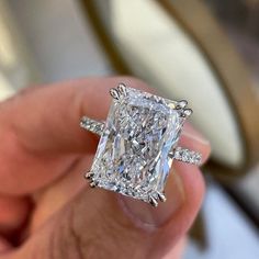 a person holding an engagement ring with a princess cut diamond in it's center