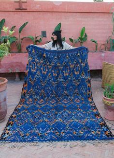 a woman sitting on top of a blue blanket next to potted plants and flowers