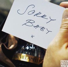 a person holding up a card that says sorry baby next to a bottle of wine