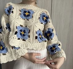 a woman wearing a crocheted sweater with blue flowers on the sleeves and shoulders