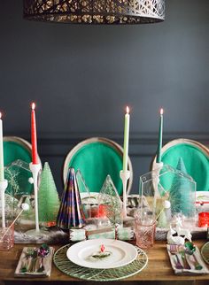 the table is set for christmas dinner with green chairs and white plates, silverware and candles