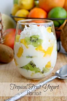 a glass filled with yogurt and fruit on top of a wooden table next to other fruits