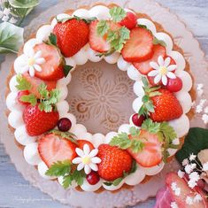 a cake decorated with strawberries and daisies on a white plate next to flowers