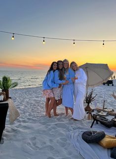 three women standing on the beach at sunset with an umbrella in front of them,