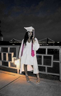 a woman in a graduation cap and gown standing on a bridge with her hand up to her ear