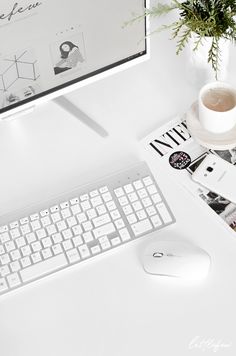 a white desk with a keyboard, mouse and plant on it next to a computer monitor