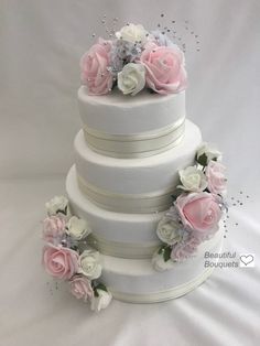 three tiered wedding cake with pink and white flowers on the top, sitting on a white tablecloth