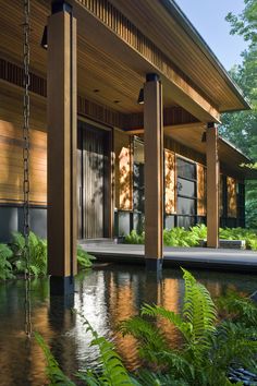 a house that is next to some water and plants in front of the house,