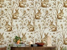 a wallpaper with rabbits and flowers on it is next to a table in front of a potted plant