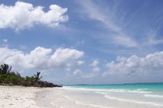 a sandy beach with blue water and white clouds