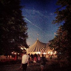 people are walking around in front of a tent at night