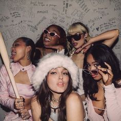 four women pose for a photo in front of a wall with writing on it and one holding a baseball bat