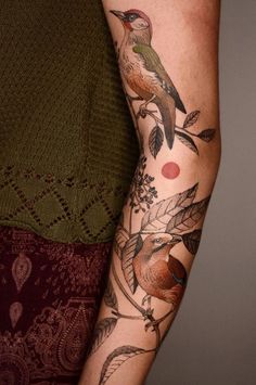 a woman's arm with tattoos on it, and a bird sitting on the branch