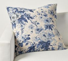 a blue and white floral pillow sitting on top of a white couch next to a wall