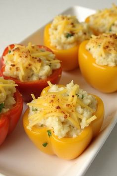 four stuffed red peppers with cheese and herbs on the top, sitting on a white plate