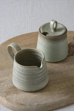 two ceramic containers sitting on top of a wooden tray