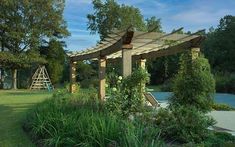 an outdoor area with a wooden pergoline and green plants on the side of it