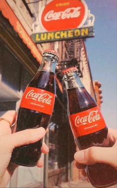 two people holding up beer bottles in front of a building