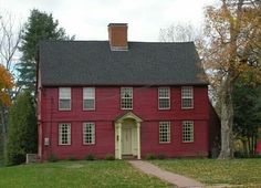 a red house with white windows and a black roof is in the middle of a grassy area