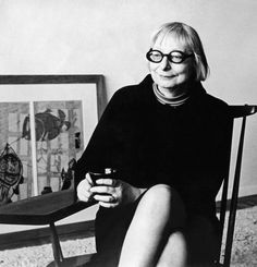 black and white photograph of a woman sitting in a chair holding a cell phone while looking at the camera