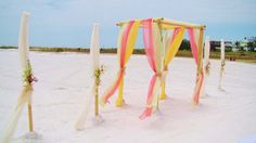 an outdoor wedding setup on the beach with white sand and colorful draping draped over it