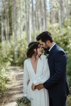 a bride and groom standing together in the woods