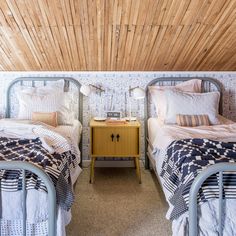 two beds in a room with wooden ceiling and wall paper on the walls behind them