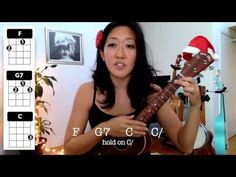 a woman is playing an ukulele with christmas decorations on the wall behind her