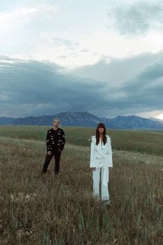 two people standing in the middle of a field with mountains in the backgroud