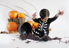 a young boy sitting on the ground next to some pumpkins and other halloween decorations