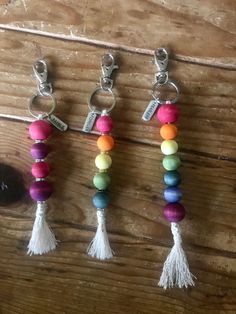 four different colored beads and tassels hanging on a wooden table next to a bottle opener