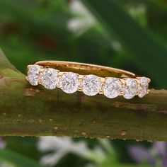 a yellow gold ring with five diamonds on it sitting on a tree branch in front of green leaves