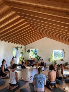 a group of people sitting on yoga mats in a room with wooden ceilings and windows