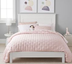 a white bed with pink comforter and two pictures on the wall above it in a bedroom