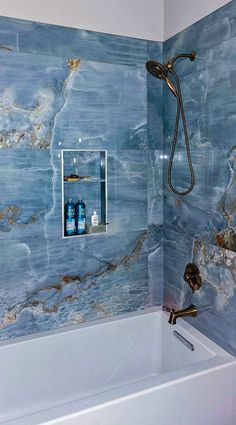 a bathroom with marbled walls and bathtub next to shower head, soap dispenser on the wall