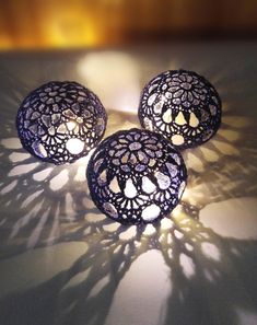 three decorative lights sitting on top of a white table next to a shadow cast wall